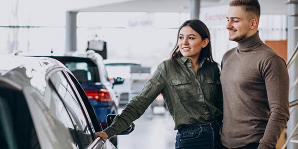 lease-vs-buy-your-first-car-is a hard choide carolina-trust-can-help-with-a-car-loan-image-of-couple shopping at car dealership