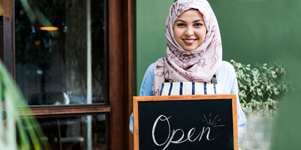 Woman-business-owner-holding-an-open-sign-in-front-of-her-store-financed-by-a-commercial-real-estate-loans.