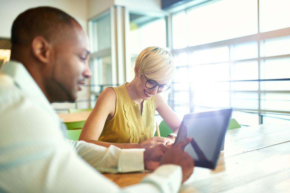 Two creative millenial small business owners working on social media strategy using a digital tablet while sitting at desk