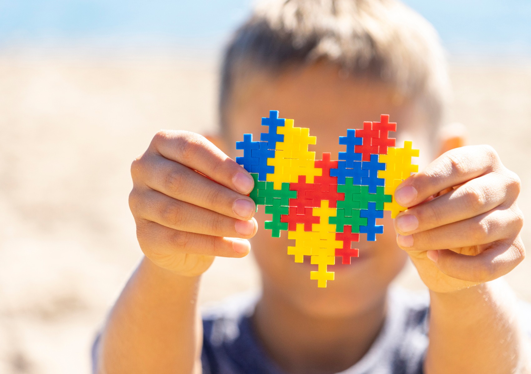 boy-holding-colorful-puzzle-heart-in-front-of-his-face-world-autism-picture-id1213546791