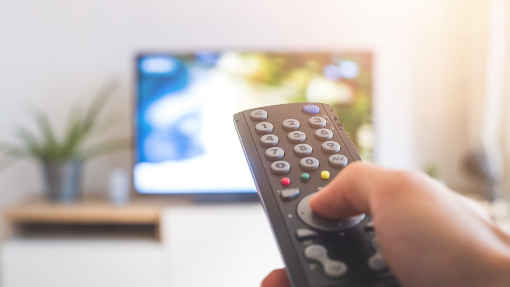 male-hand-is-holding-tv-remote-control-streaming-on-a-smart-tv-picture-id1285286170