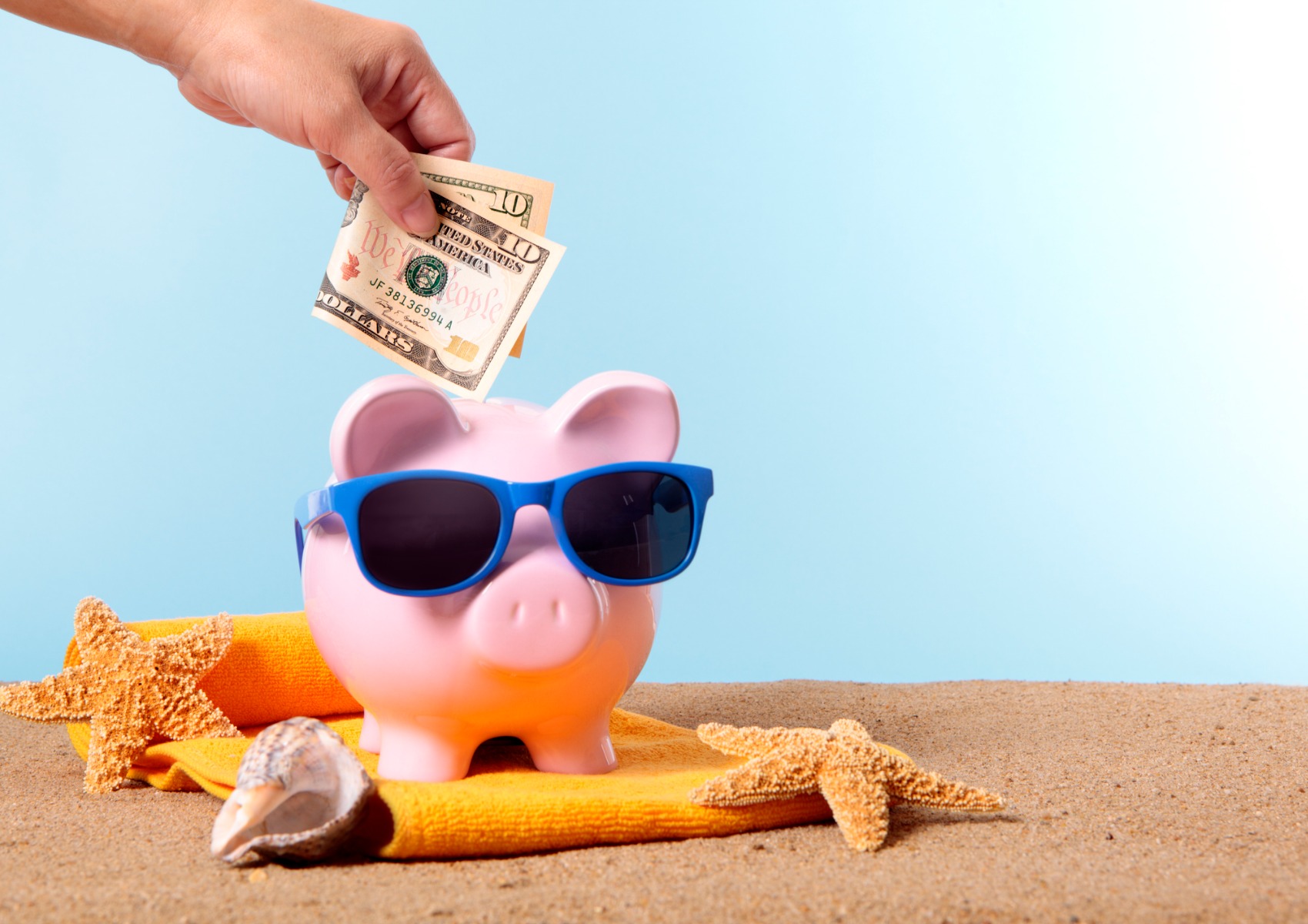 pink-piggy-bank-with-beach-items-and-money-being-put-in-picture-id166513010