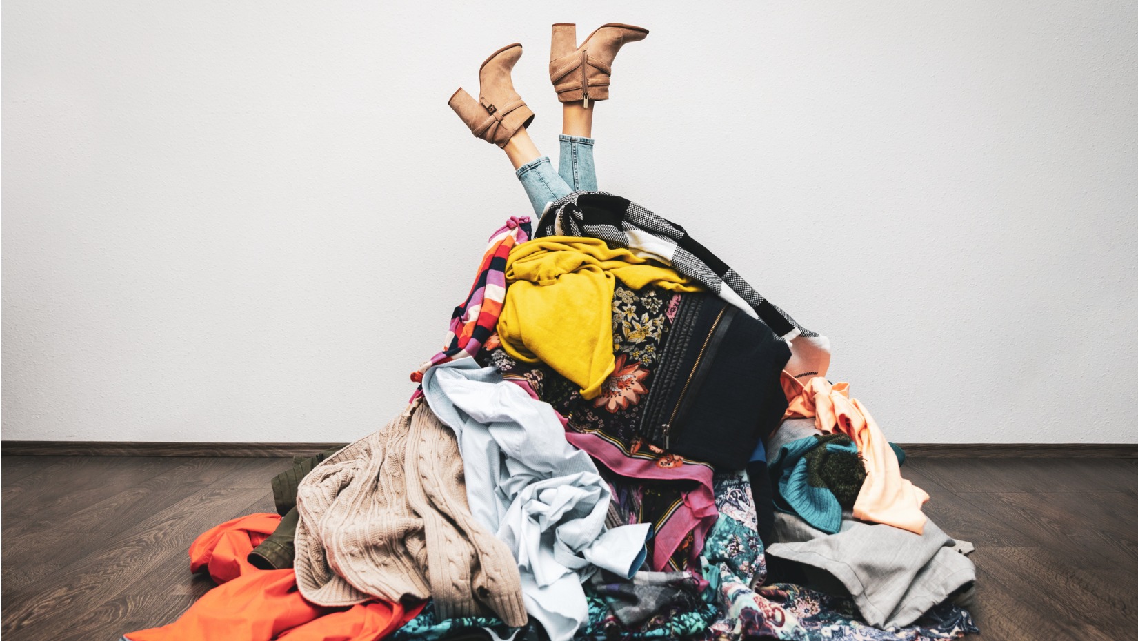 woman-legs-out-of-a-pile-of-clothes-on-the-floor-shopping-addiction-picture-id1190179908