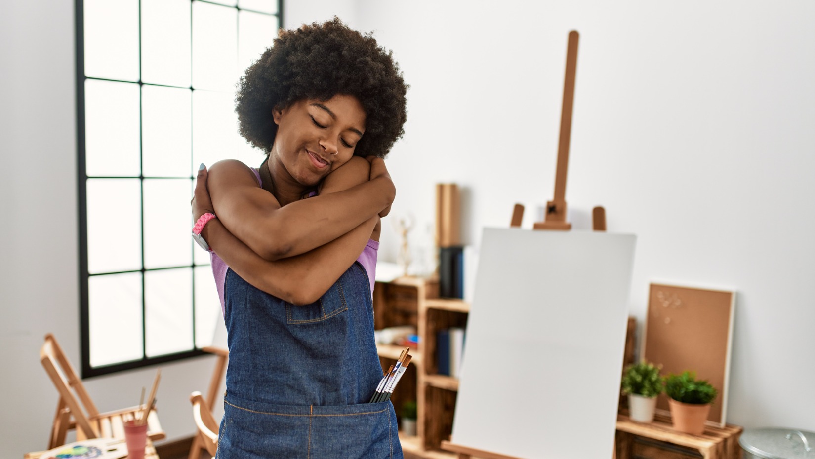 young-african-american-woman-with-afro-hair-at-art-studio-hugging-picture-id1327848957